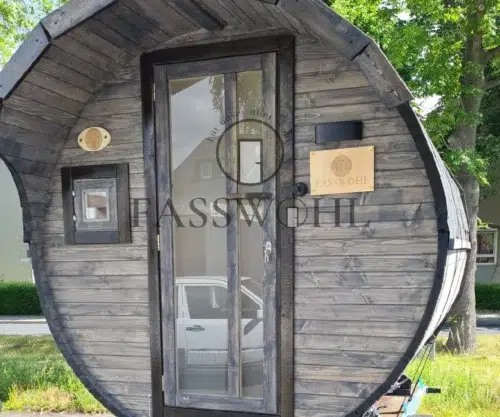 Eine Fasswohl Fasssauna aus grauem Holz steht im Garten