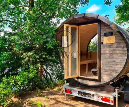 Das Saunafass steht mit offener Tür auf einem Hügel