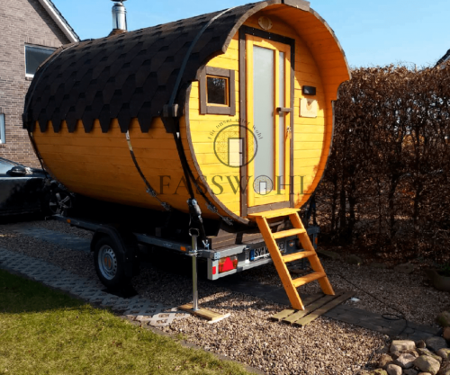 Eine Fasssauna auf Vollfundament, die von der Sonne bestrahlt wird und im Garten eines Kunden steht