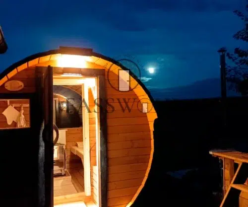 Eine beleuchtete Fasssauna bei Nacht