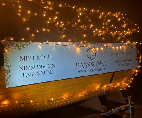 Eine Fasswohl Fasssauna behangen mit vielen Stecklichtern und Weihnachtsketten