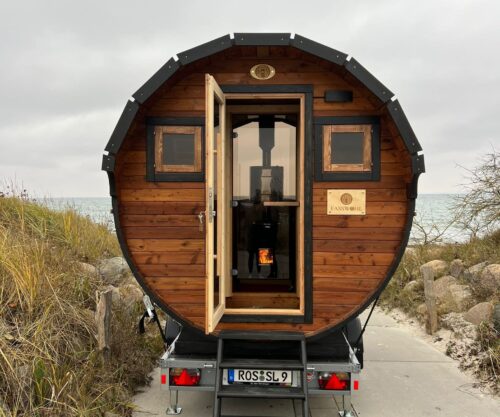 Eine Fasssauna mit offener Tür auf einem Anhänger auf einem schmalen Weg
