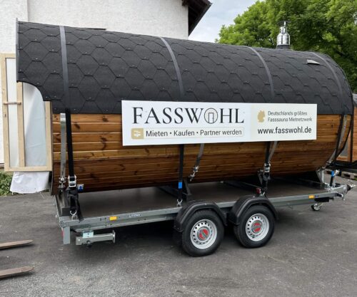 Eine Fasssauna mit großem "Fasswohl" Schild auf einem Anhänger